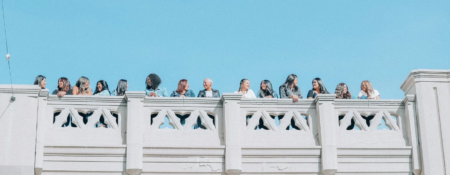 a line of women of mixed ethnicities stood on a bridge in a long line